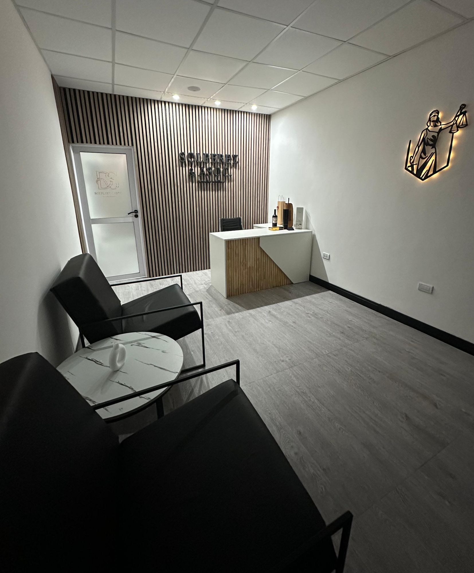 Recepción del estudio en Bahía Blanca: sillones negros, mesa de mármol y la Dama de la Justicia retroiluminada sobre una pared de listones de madera.